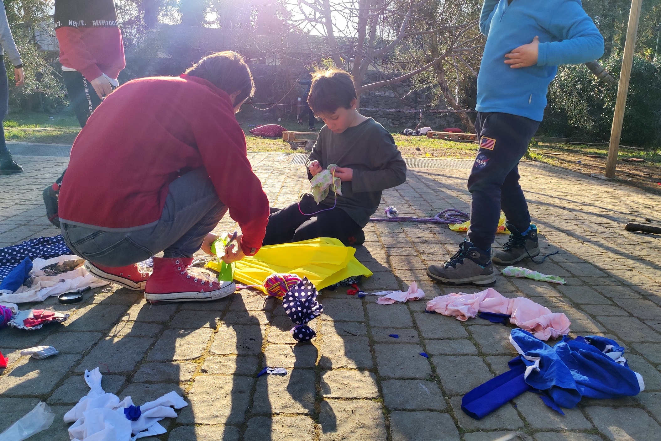 In giardino i bambini costruiscono comete con stoffe e carta pesta insieme a un'adulta