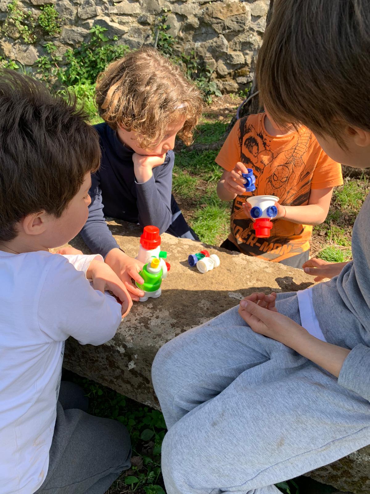 Bambini che creano sculture con vasetti e tappi di plastica.