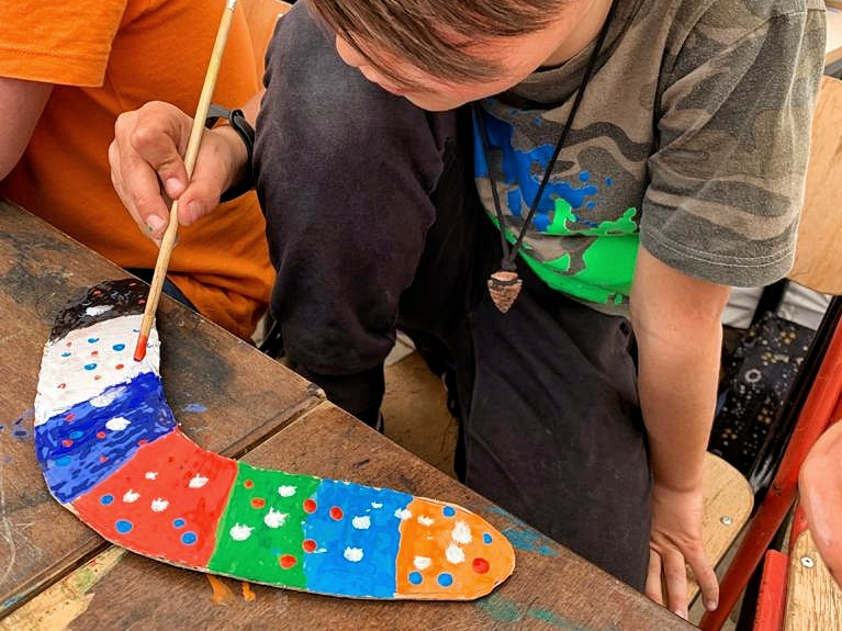 Un bambino decora con le tempere il boomerang che ha creato col cartone