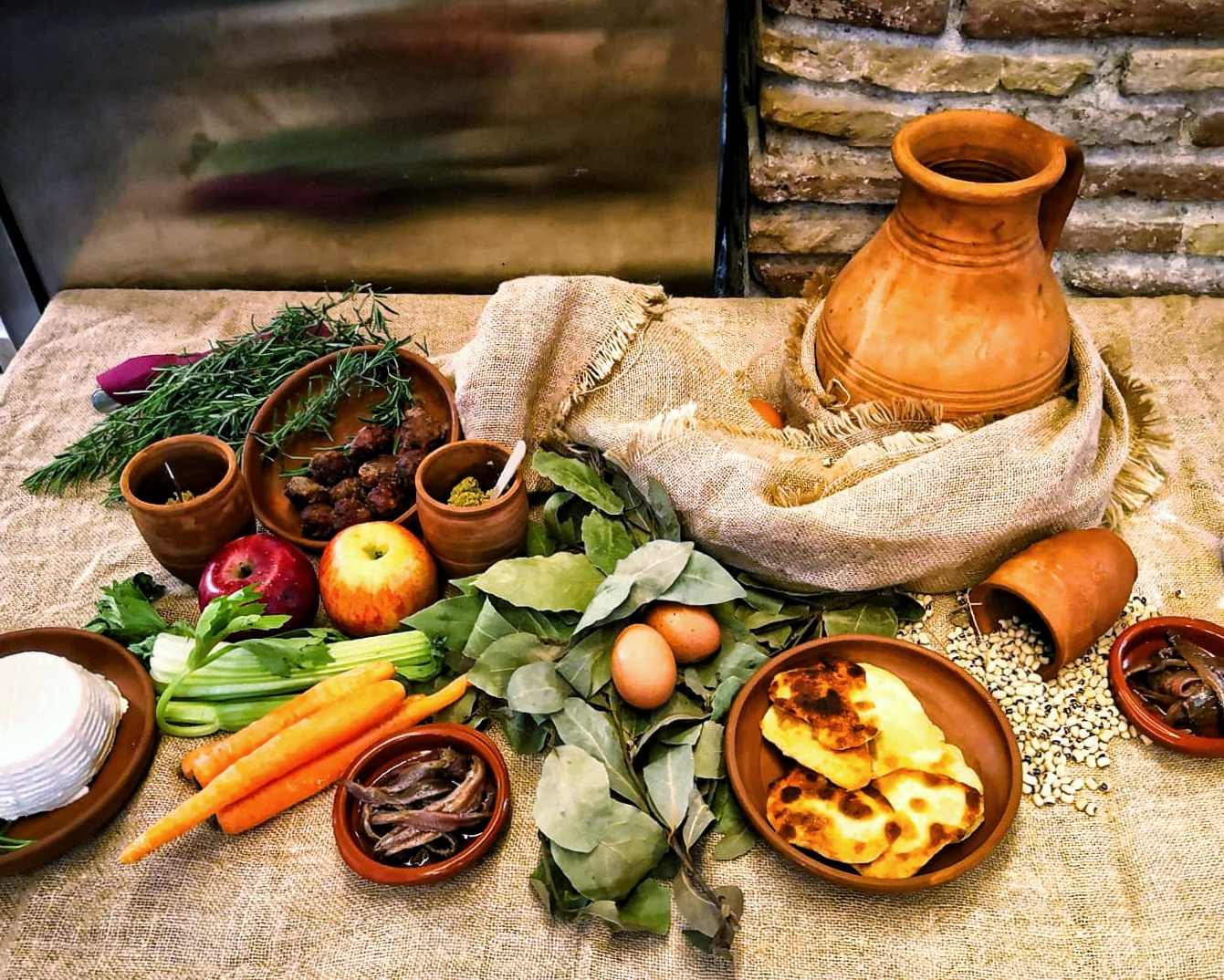Una tavola apparecchiata con stoffe rustiche, anfore e piatti di coccio per offrire ai bambini le pietanze tipiche dell'antica gustatio romana: verdure, polpette, formaggi, legumi e torte salate