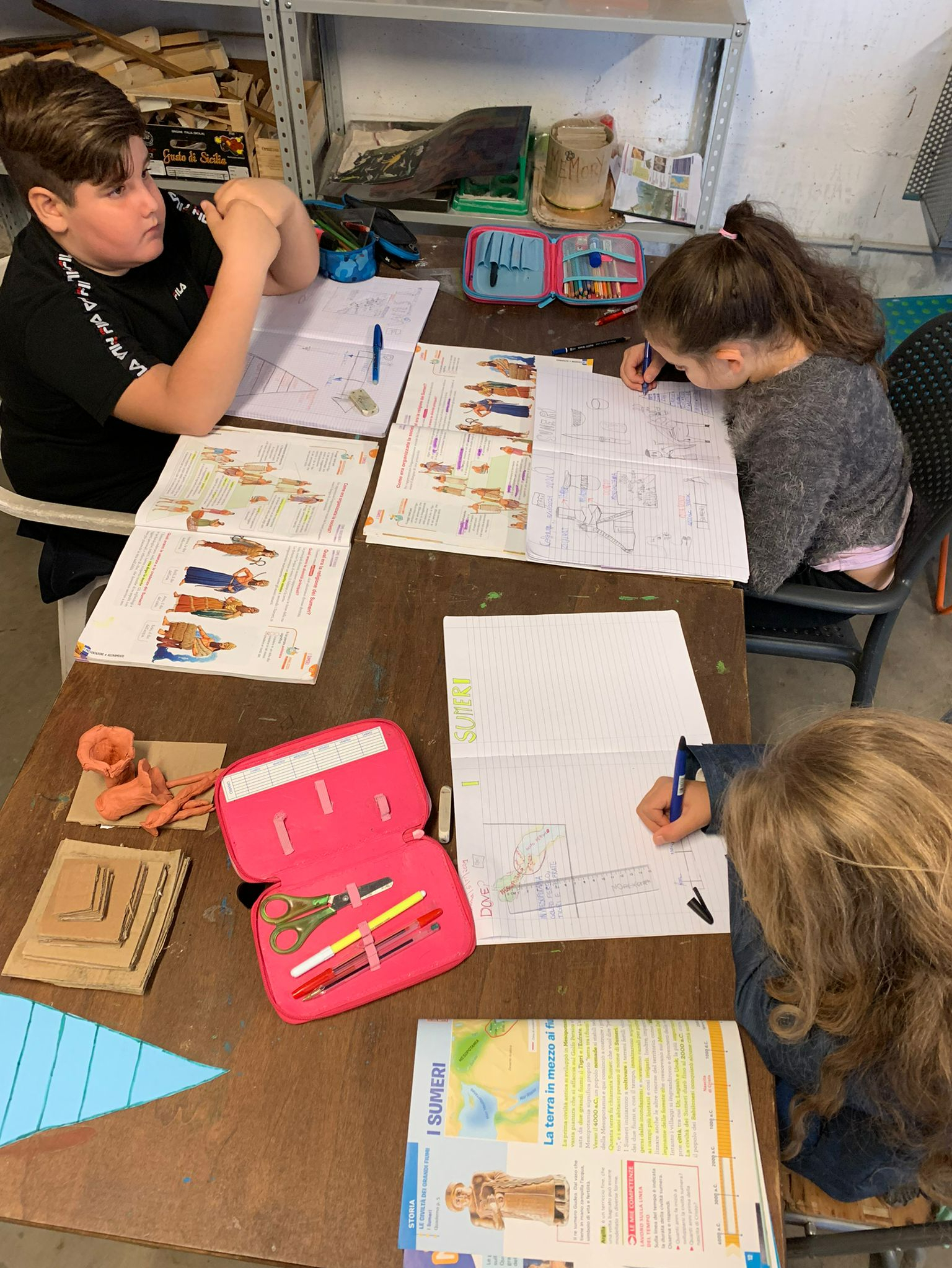 Due bimbe e un bimbo stanno studiano le civiltà antiche sui loro libri e quaderni.